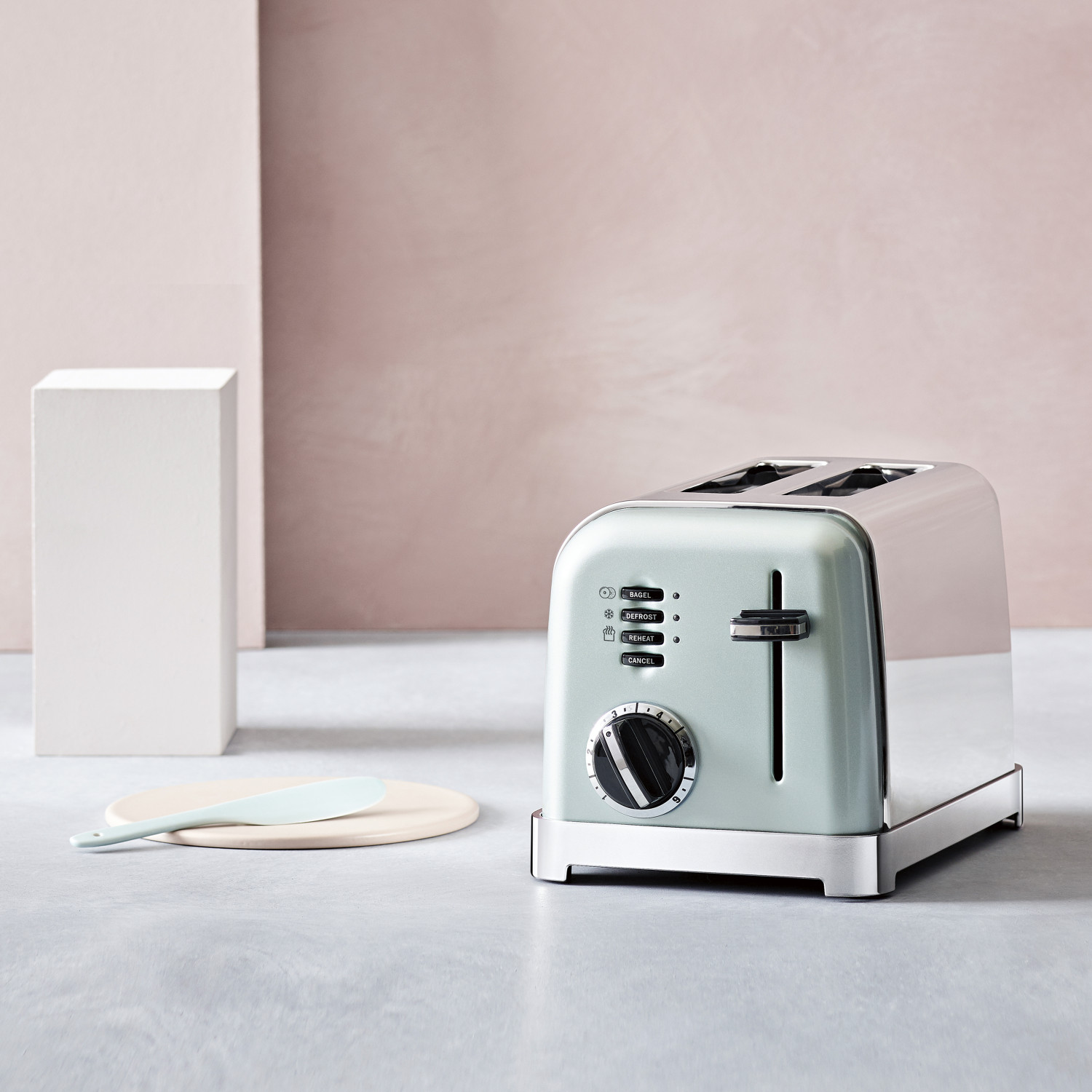Ein hellgrüner Toaster steht auf einem grauen Tisch neben einem weißen Würfel.
