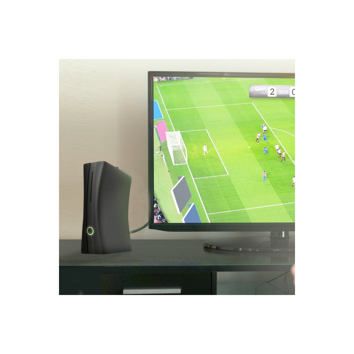 Una consola de videojuegos negra junto a un televisor que muestra un partido de fútbol.