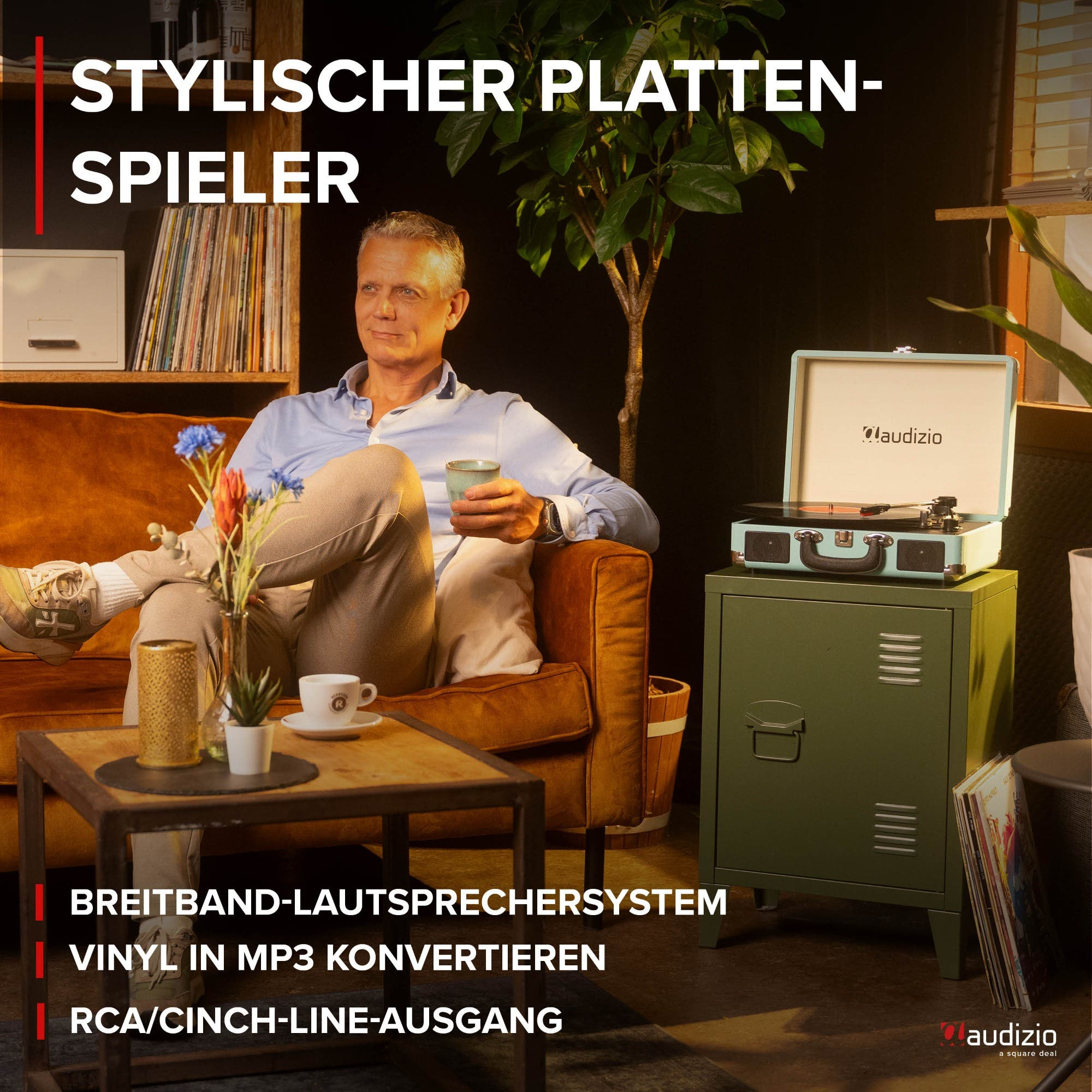 Mann sitzt auf Sofa, hält Tasse; Plattenspieler steht auf Schrank.
