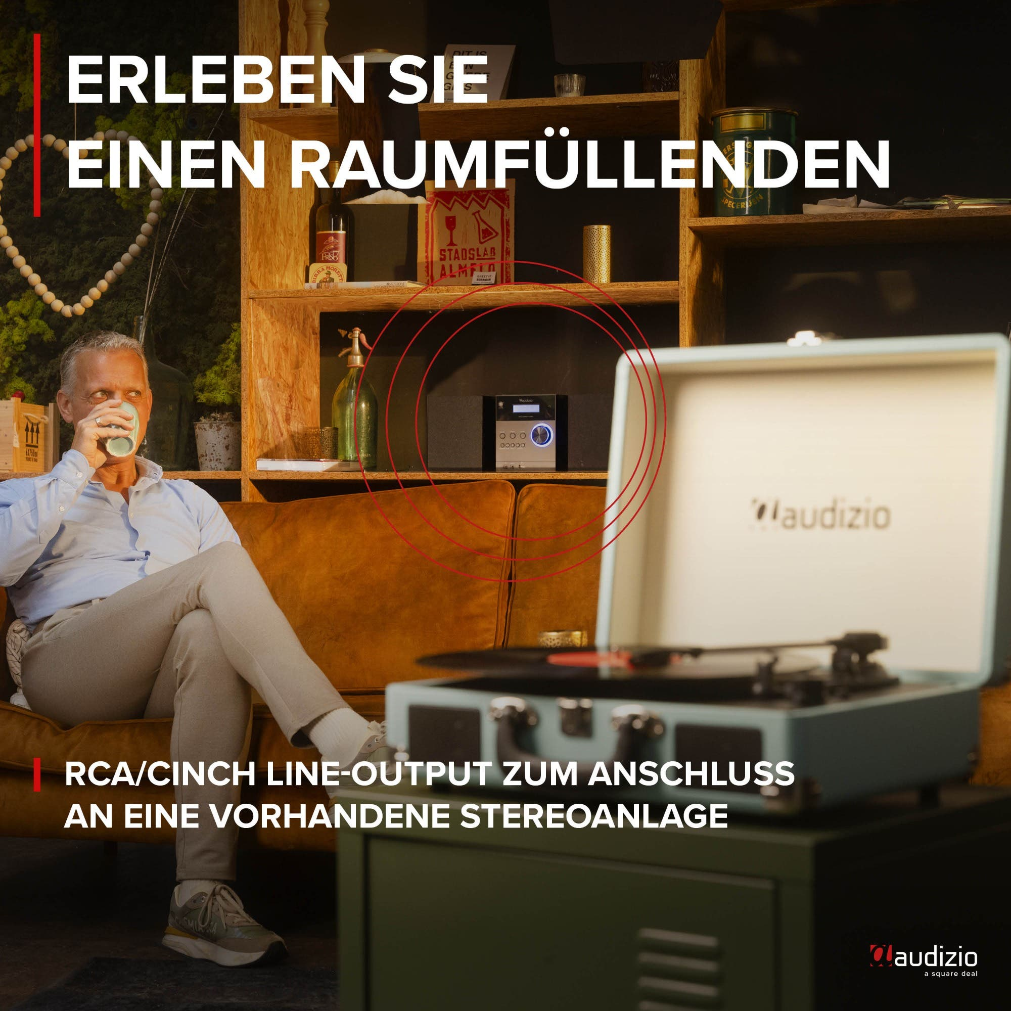 Mann sitzt auf Sofa, trinkt aus Tasse. Plattenspieler und Musiksystem im Vordergrund.