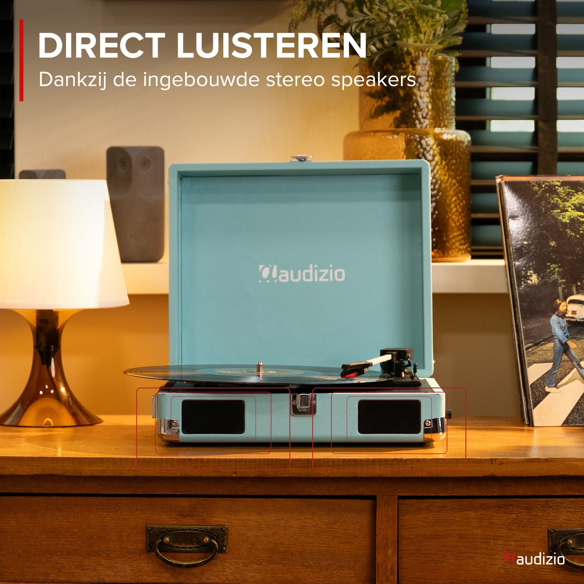 Un tocadiscos-radio azul claro con vinilo y lámpara sobre mueble de madera.
