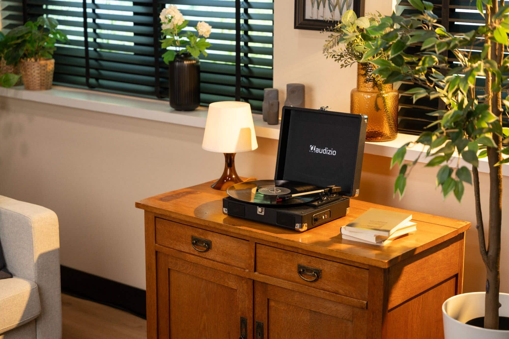 A record player sits on a wooden cabinet next to a lamp and plants.