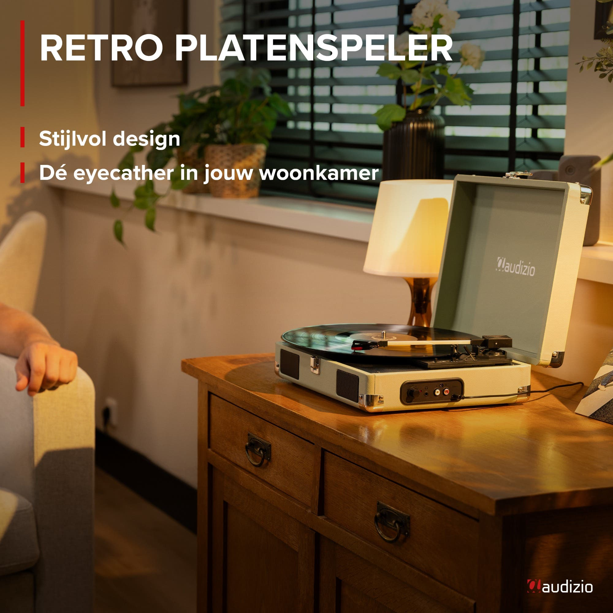 A retro record player on a wooden table. Armchair on the left, lamp on the right.