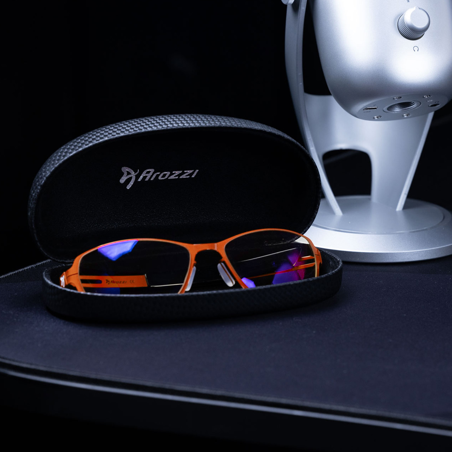 Orange Brille in einem schwarzen Kasten neben einem silbernen Mikrofon.