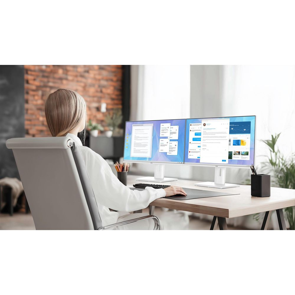 Una donna con i capelli biondi corti è seduta a una scrivania, guardando due monitor.