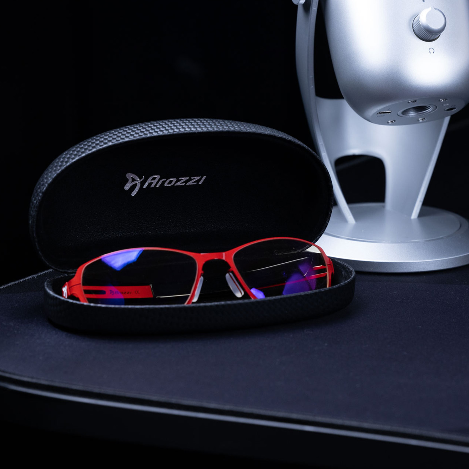 Rote Brille in schwarzem Kasten neben Silbermikrofon.