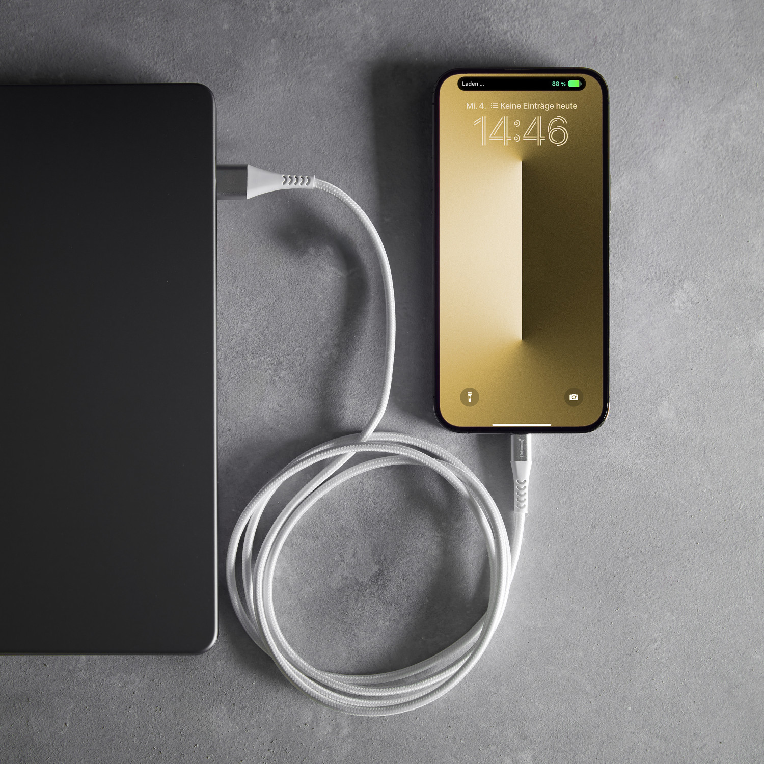 Un câble de chargement blanc relie un smartphone à un ordinateur portable sur une surface grise.