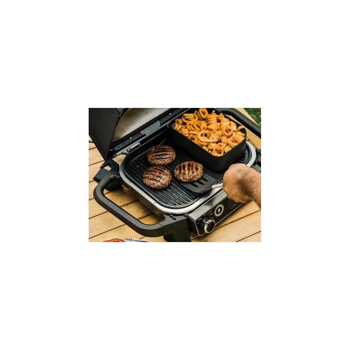 Drie hamburgers worden gegrild naast een bakje krulfriet op een houten ondergrond.
