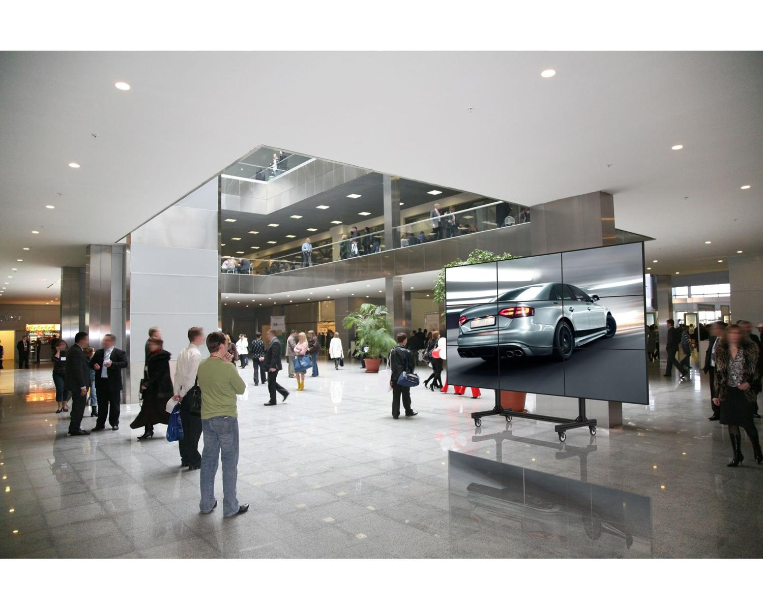 Ein silbernes Auto wird auf einer großen Videowand in einer belebten Lobby gezeigt.