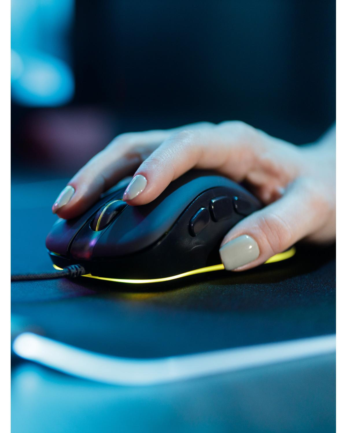 Una mano con unghie grigie usa un mouse da gaming nero con illuminazione LED gialla.