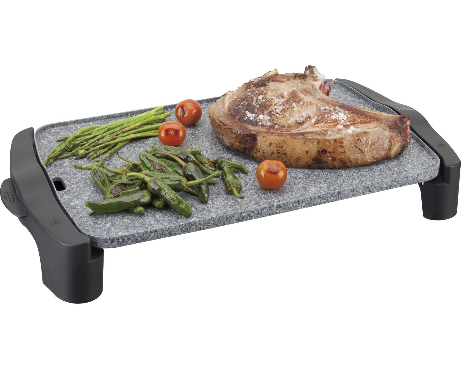 Un filete con espárragos, pimientos y tomates cherry en una parrilla de piedra.