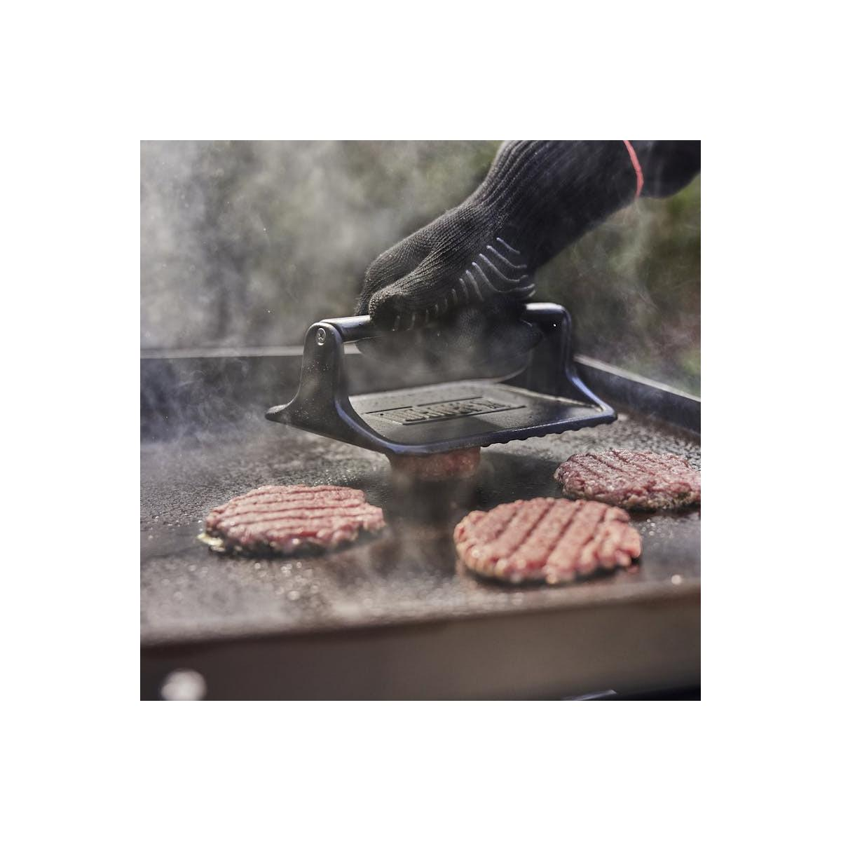 Hamburguesas siendo presionadas en una parrilla con una prensa.