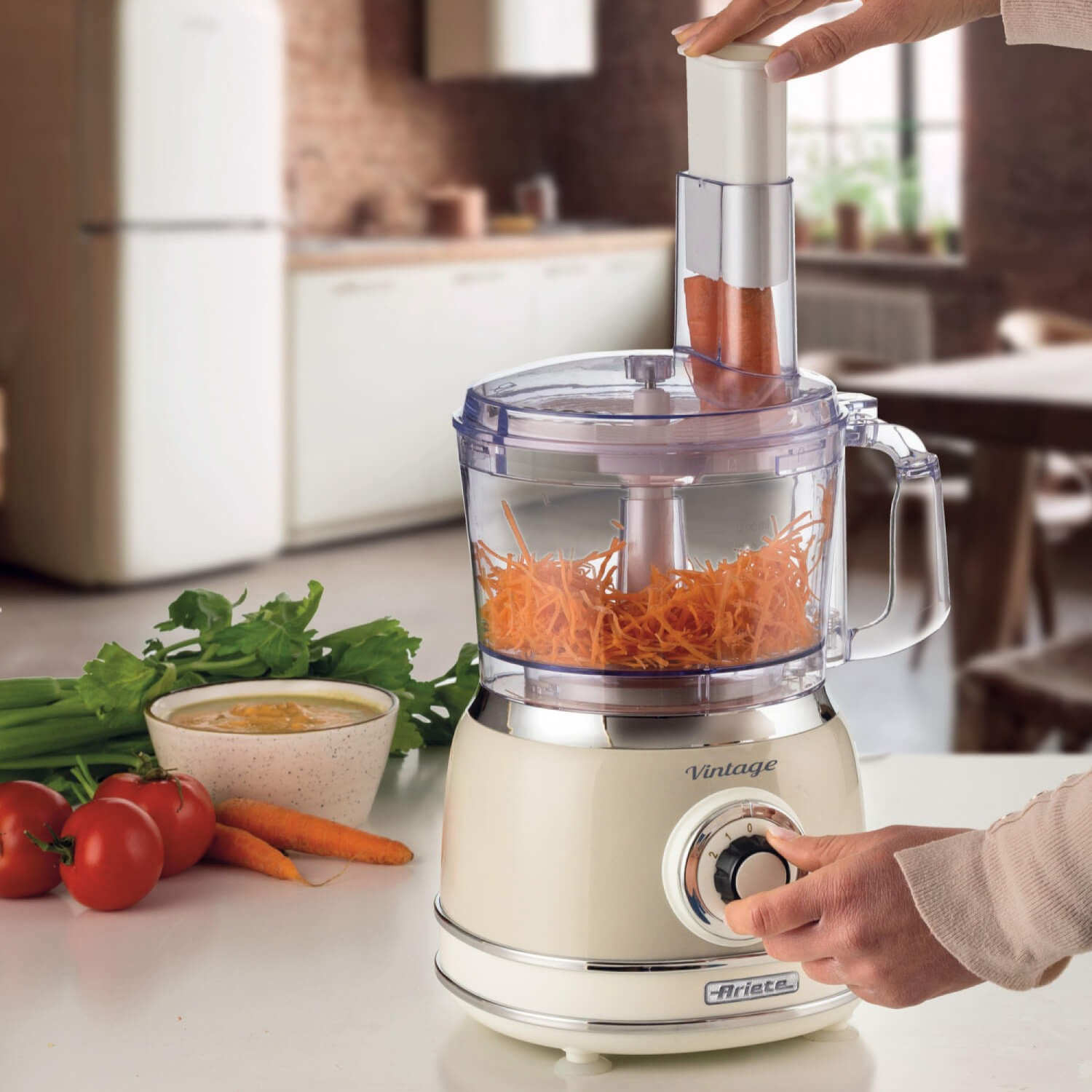 Un robot da cucina retrò grattugia carote. Pomodori, sedano e salsa sono vicini.