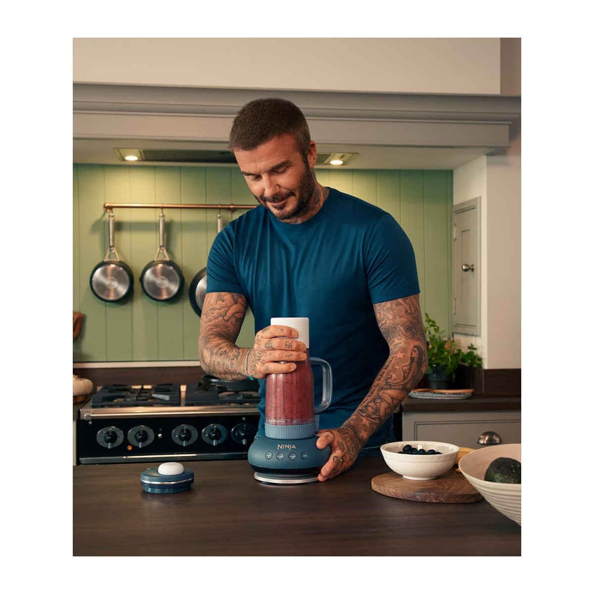 Ein Mann mit Tattoos mixt ein rotes Getränk in einem Mixer in einer Küche.