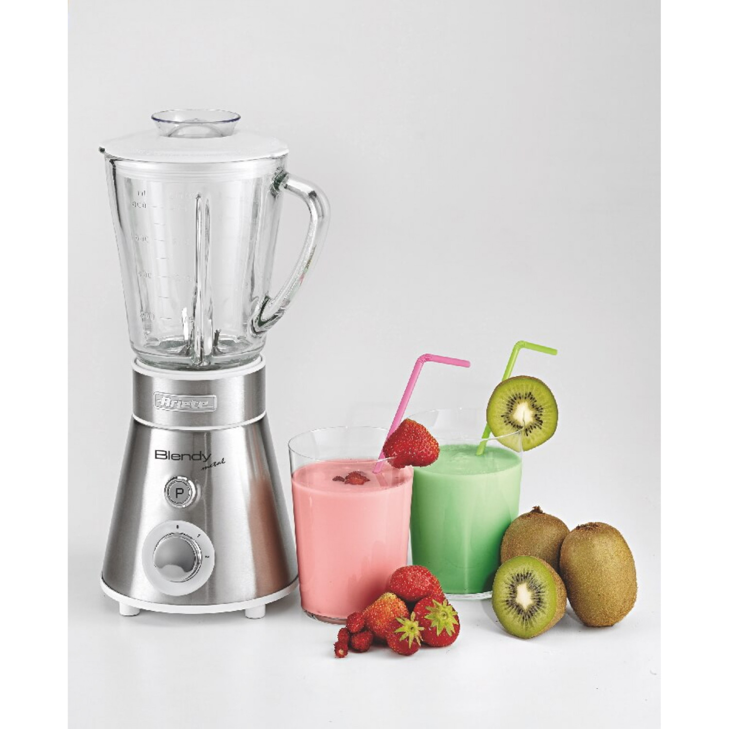 Una licuadora plateada junto a dos vasos de batidos, fresas y kiwis.