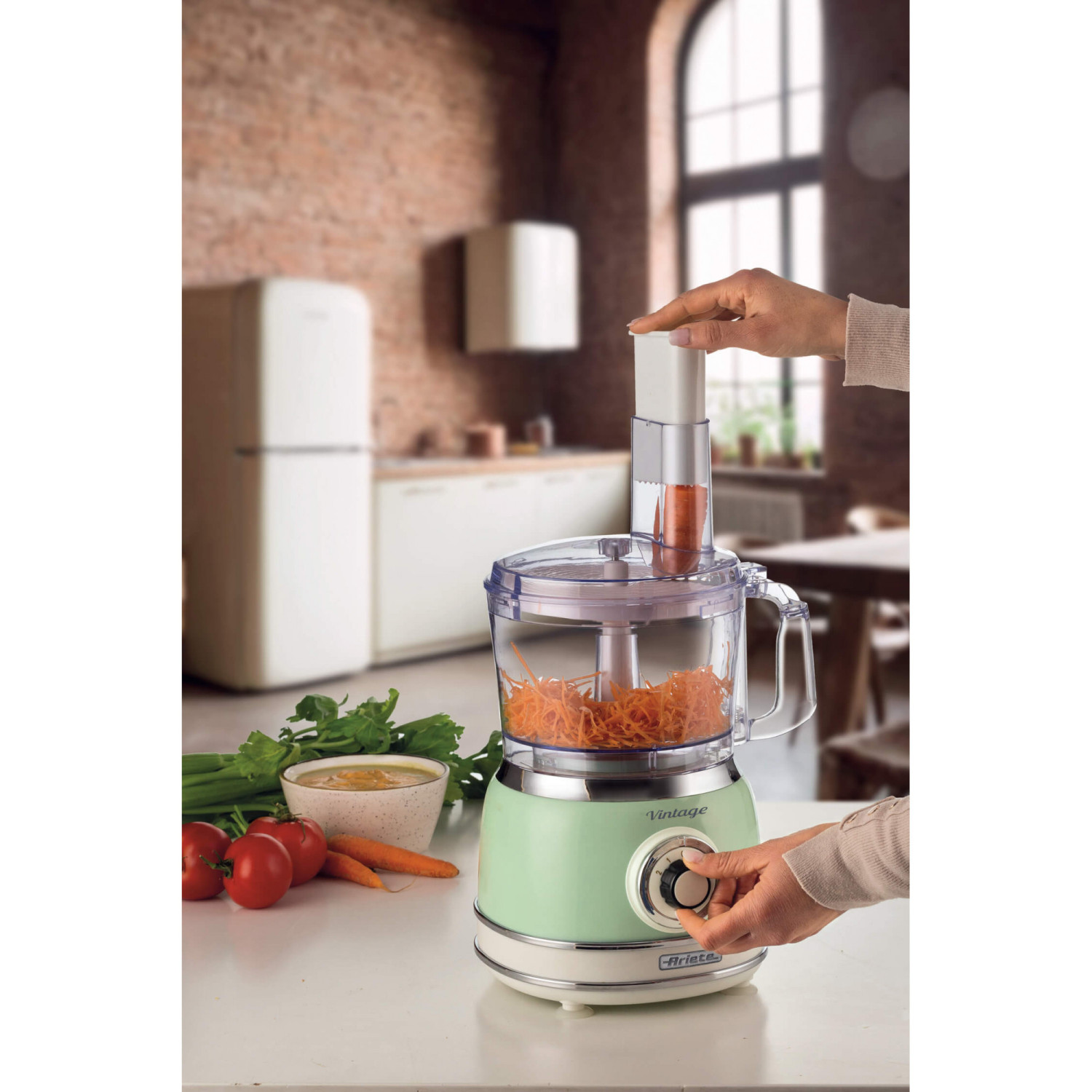 Una mano usa un robot da cucina per tritare le carote. Verdure e una ciotola sono vicine.