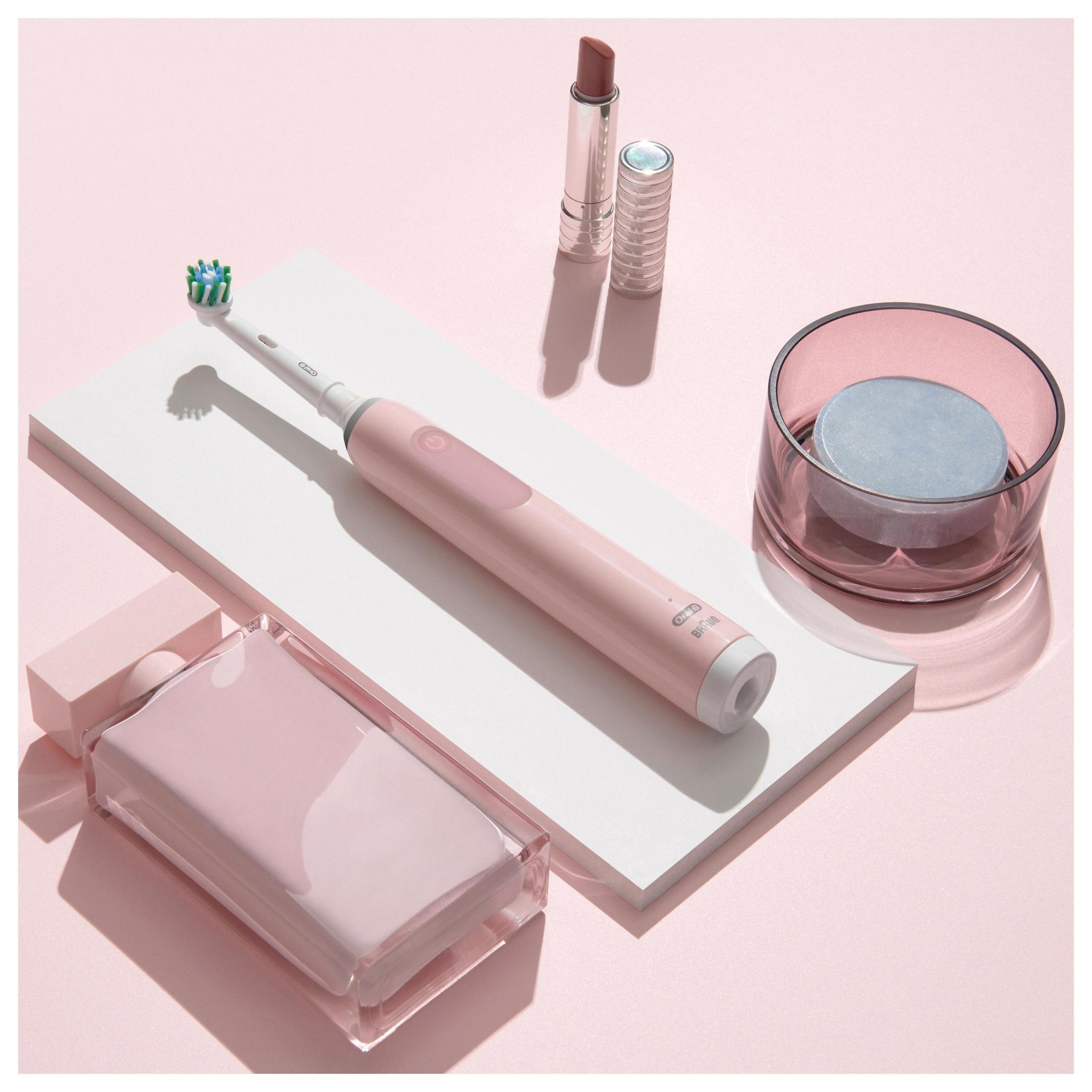 Un cepillo de dientes eléctrico rosa, lápiz labial y jabón sobre fondo rosa.