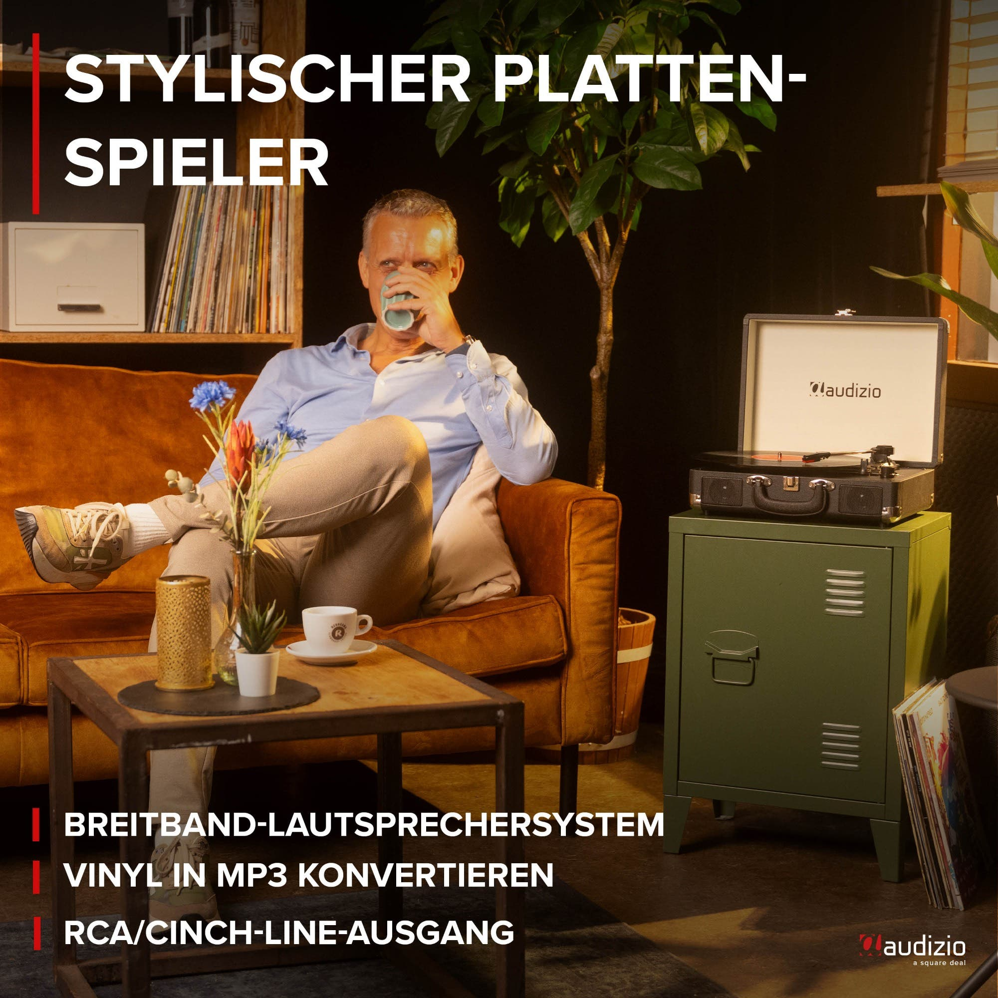 Man sits on a brown sofa drinking from a mug, next to a record player.