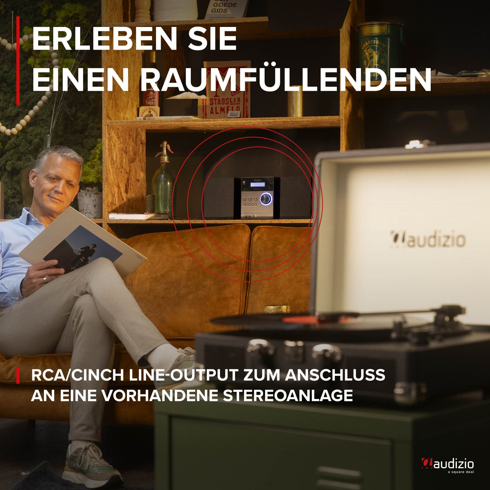 Man sits on sofa with record, turntable, and audio device on shelf.
