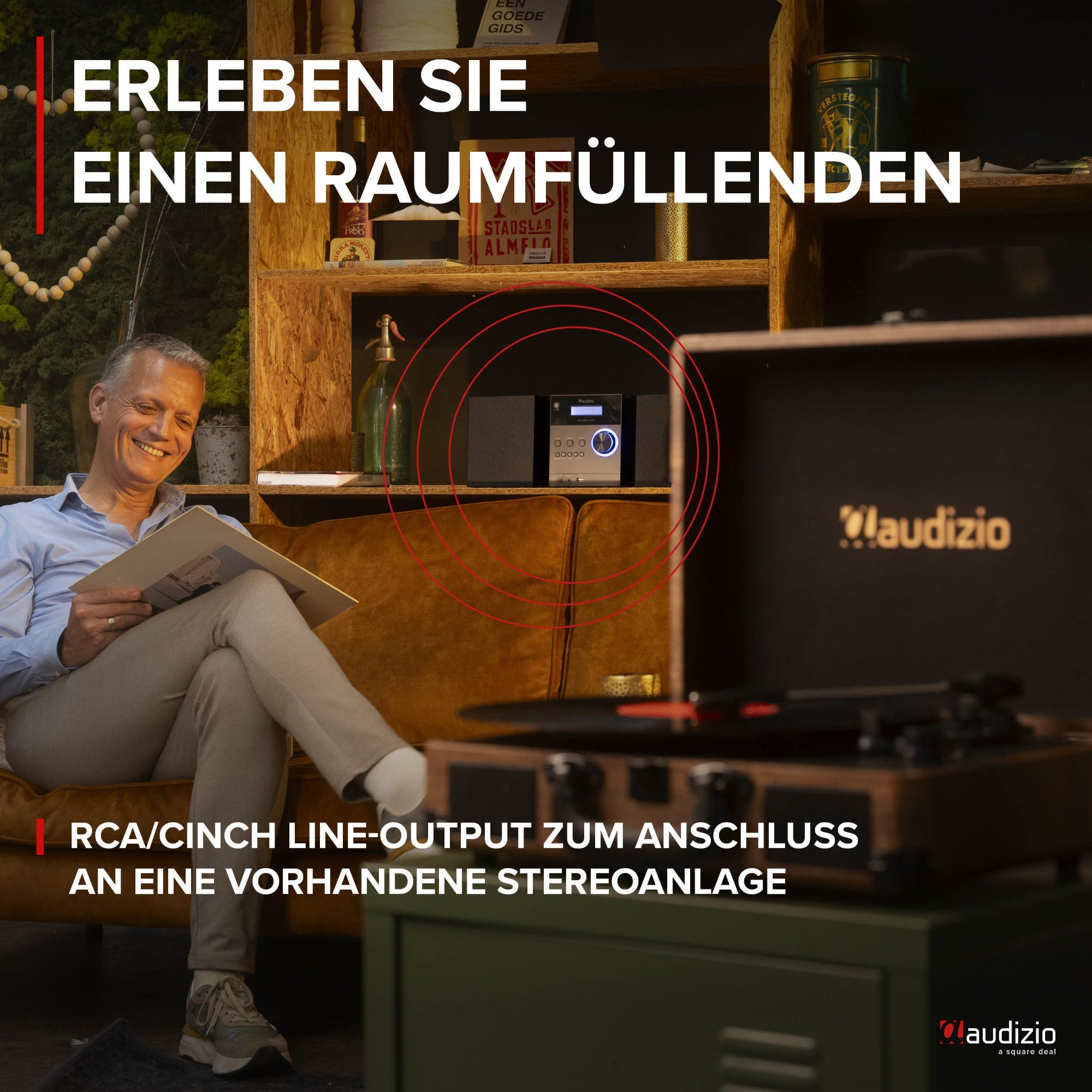 Mann auf Sofa liest Platte. Hifi-Anlage auf Regal. Plattenspieler.
