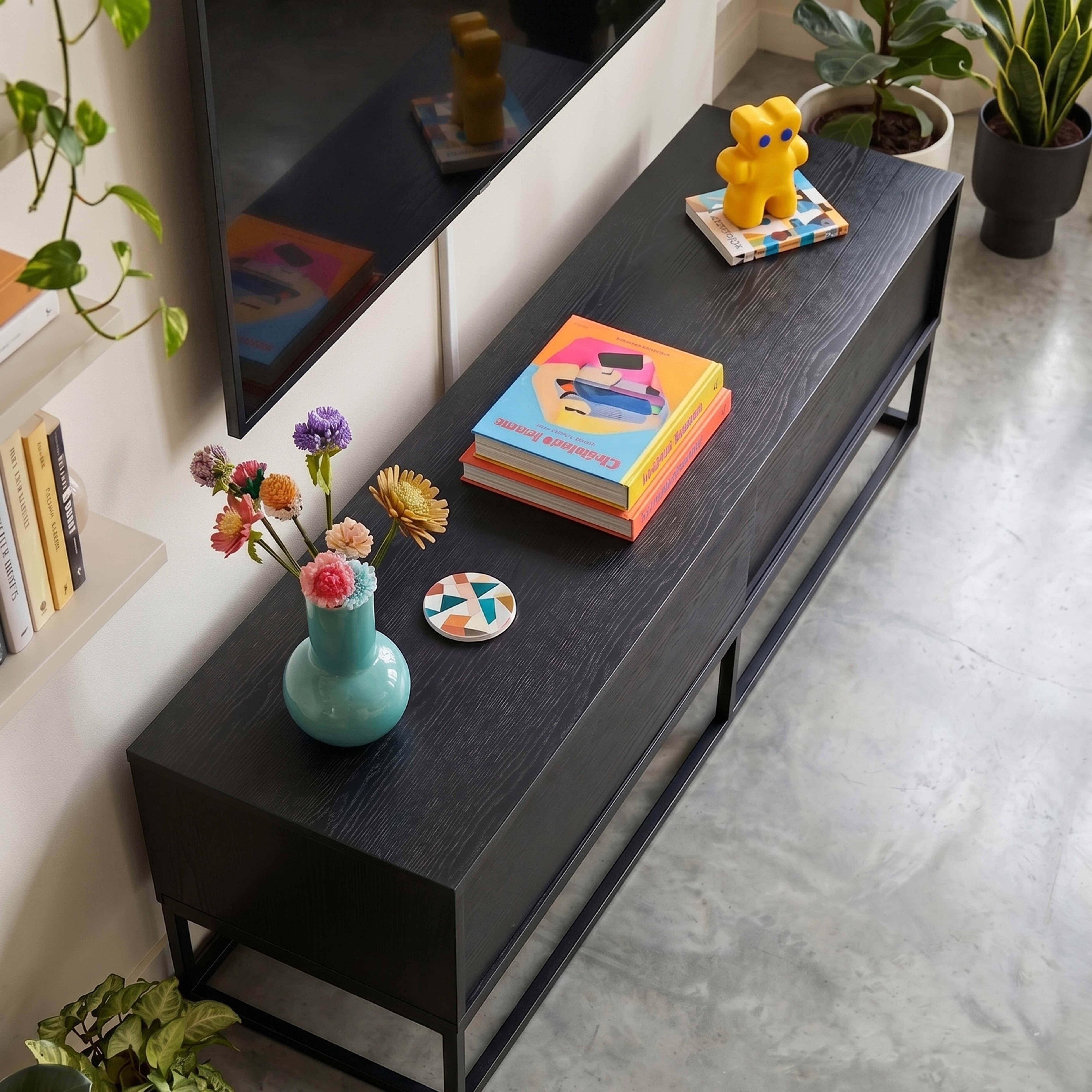 Ein gelber Bär steht auf Büchern neben einer Vase mit Blumen auf einem schwarzen Schrank.