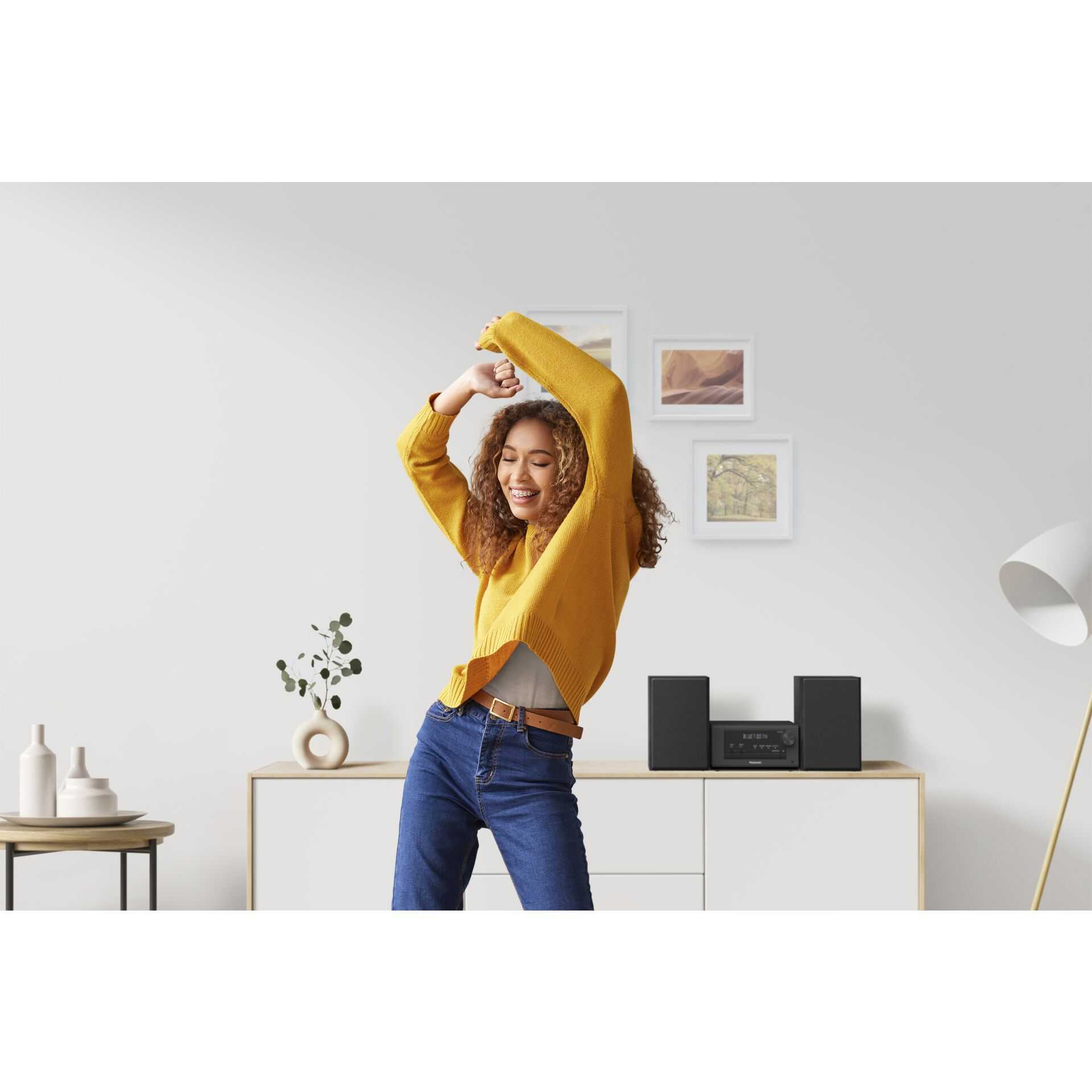 Frau tanzt in gelbem Pullover und Jeans im Wohnzimmer mit Stereoanlage.