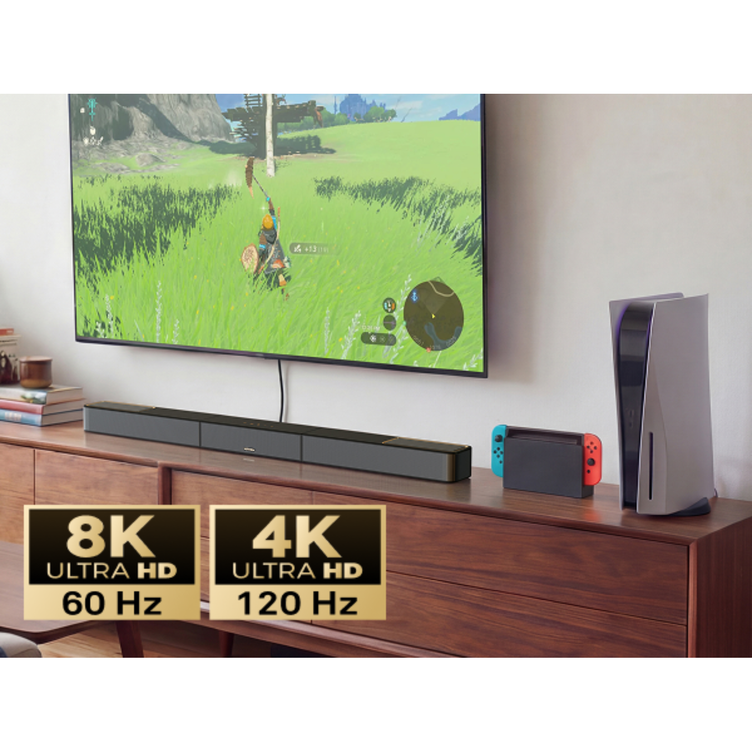 Une TV affiche un jeu vidéo. Une barre de son, une console et un système de jeu sont sur une commode en bois.