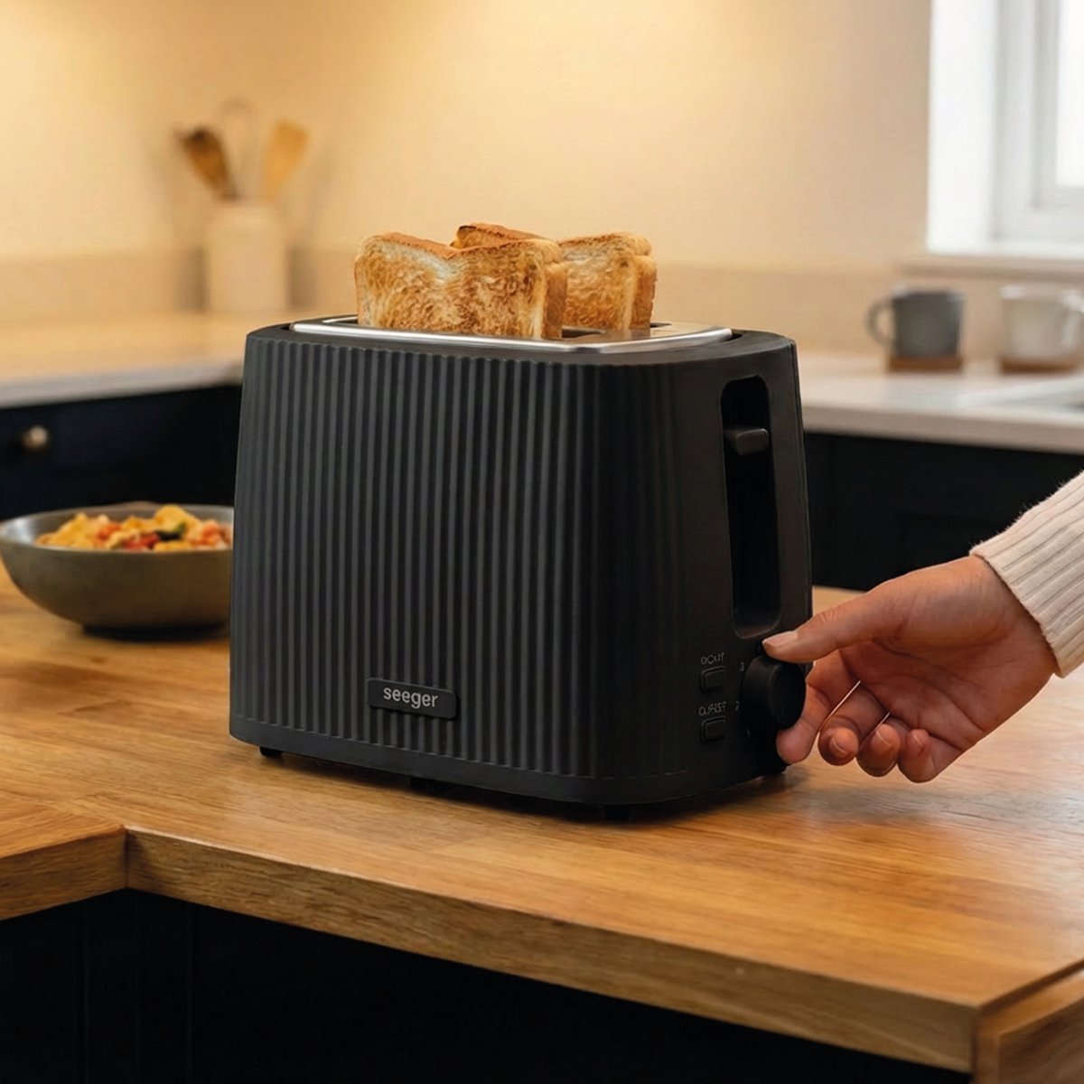 Black toaster with three toasted bread slices. Bowl of food in background.