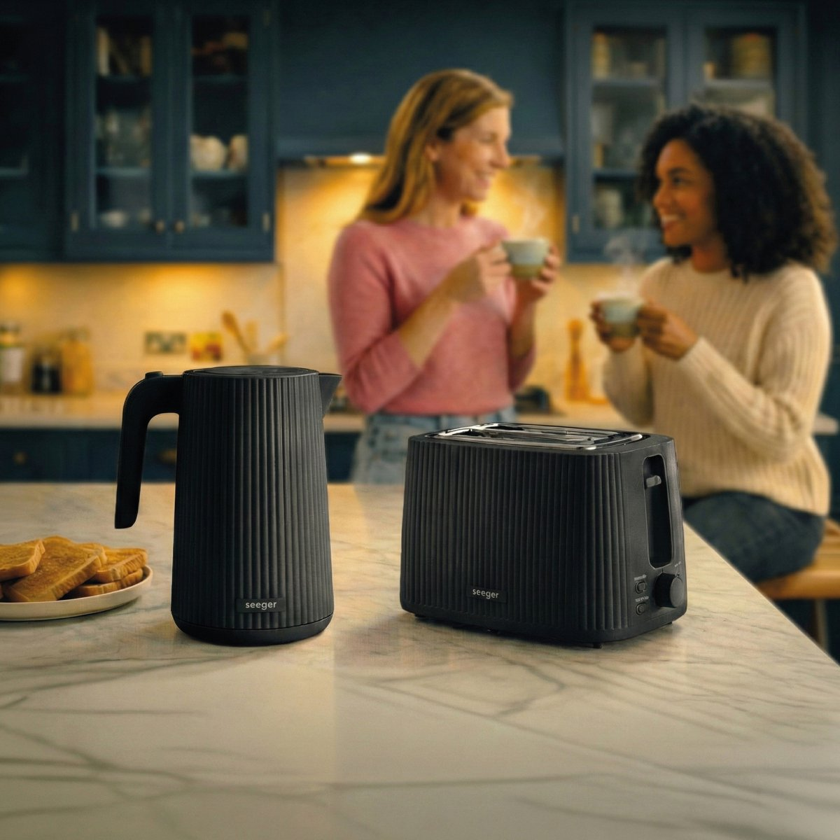 Black kettle and toaster on marble counter, two women drink coffee in the background.