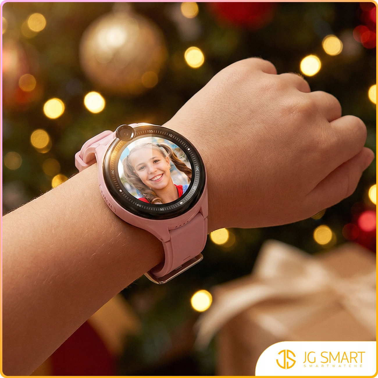 Różowy smartwatch na nadgarstku dziecka pokazuje zdjęcie uśmiechniętej dziewczynki. Choinka w tle.