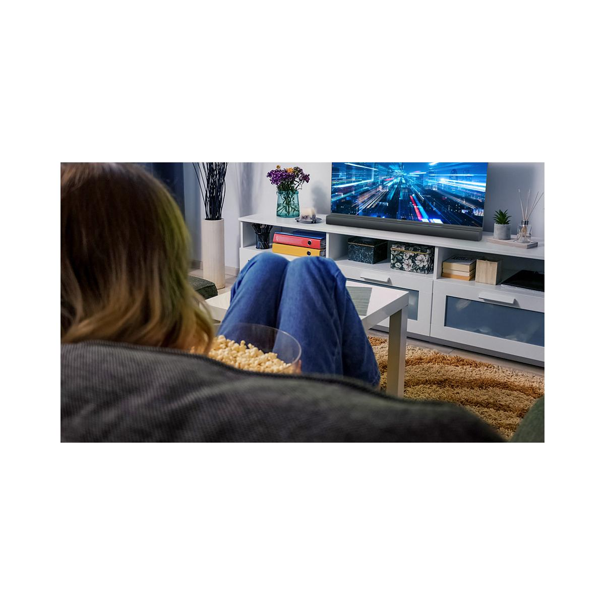 Eine Person isst Popcorn und schaut fern. Das Bild zeigt einen Fernseher.