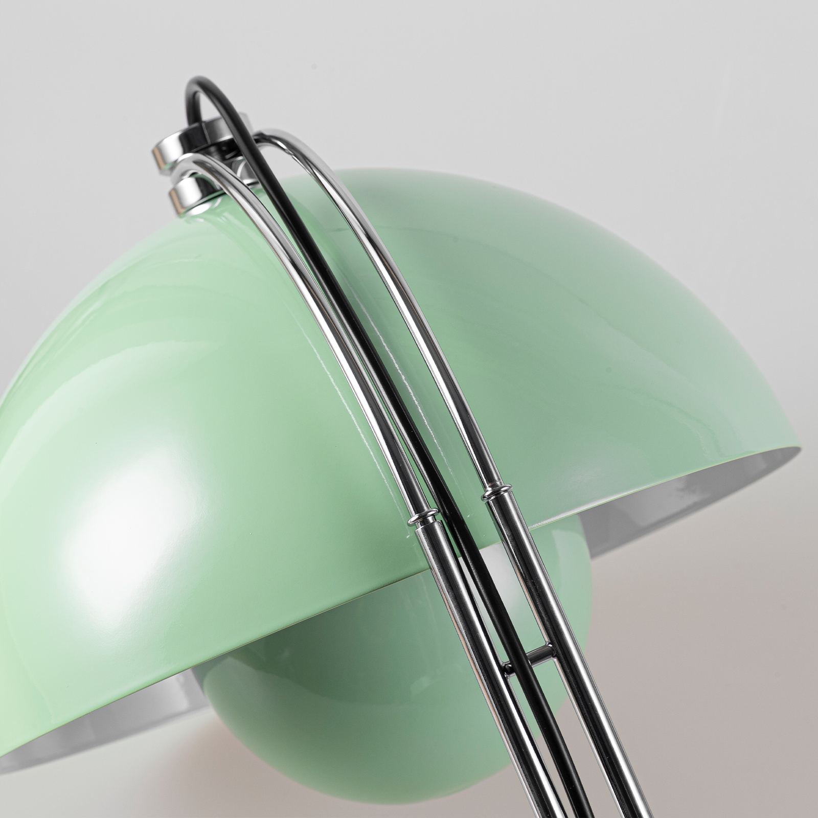 Una pantalla de lámpara verde claro de metal con brazos articulados plateados sobre fondo gris.