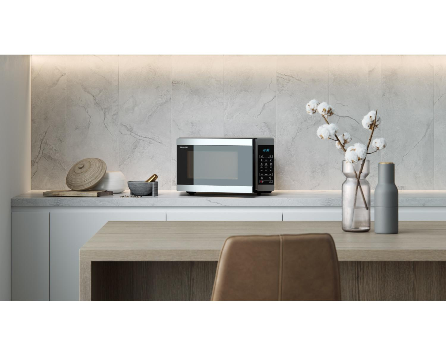 Un microondas Sharp plateado está sobre una encimera de cocina, junto a objetos decorativos.