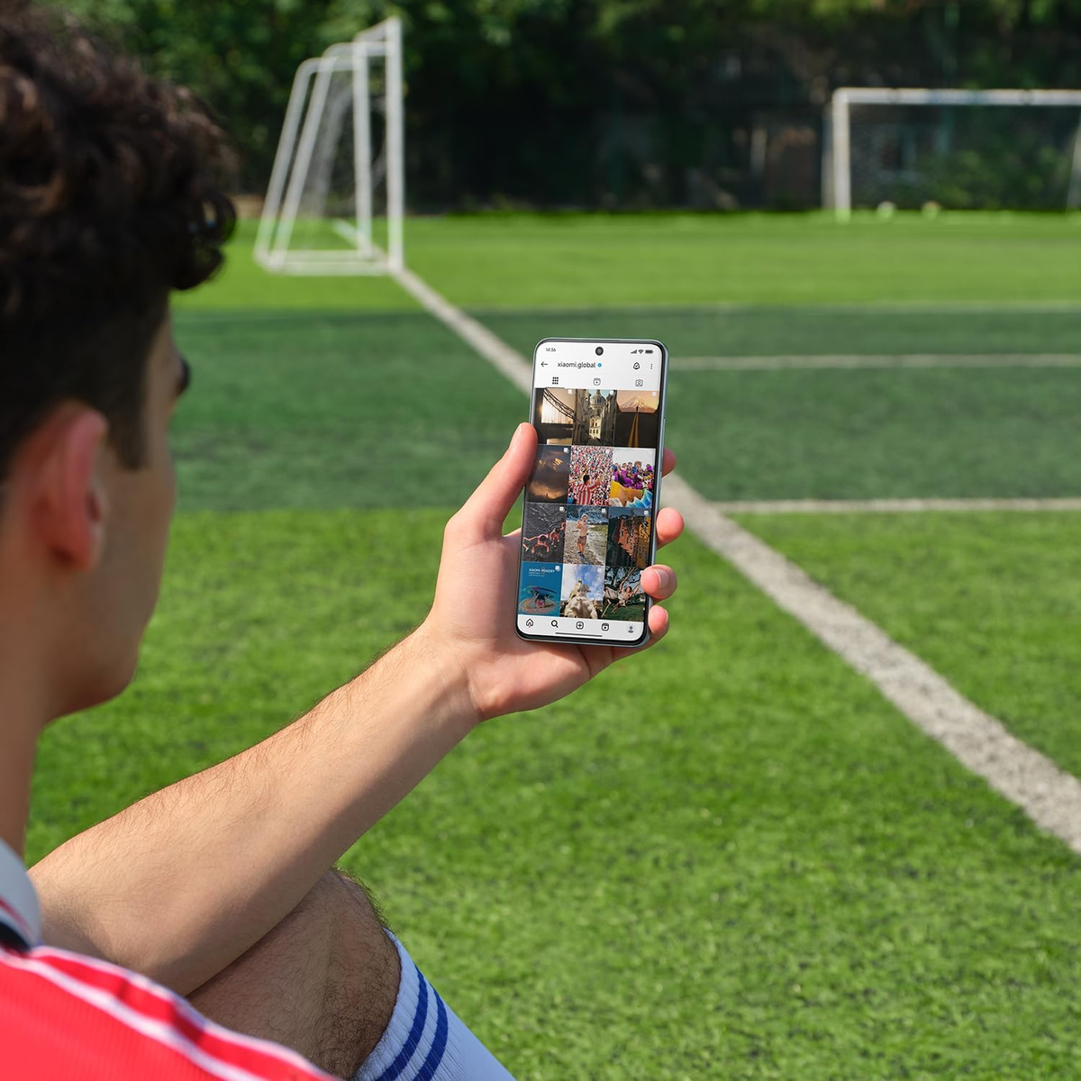 Mann hält Smartphone mit Instagram-Feed auf Fußballplatz.