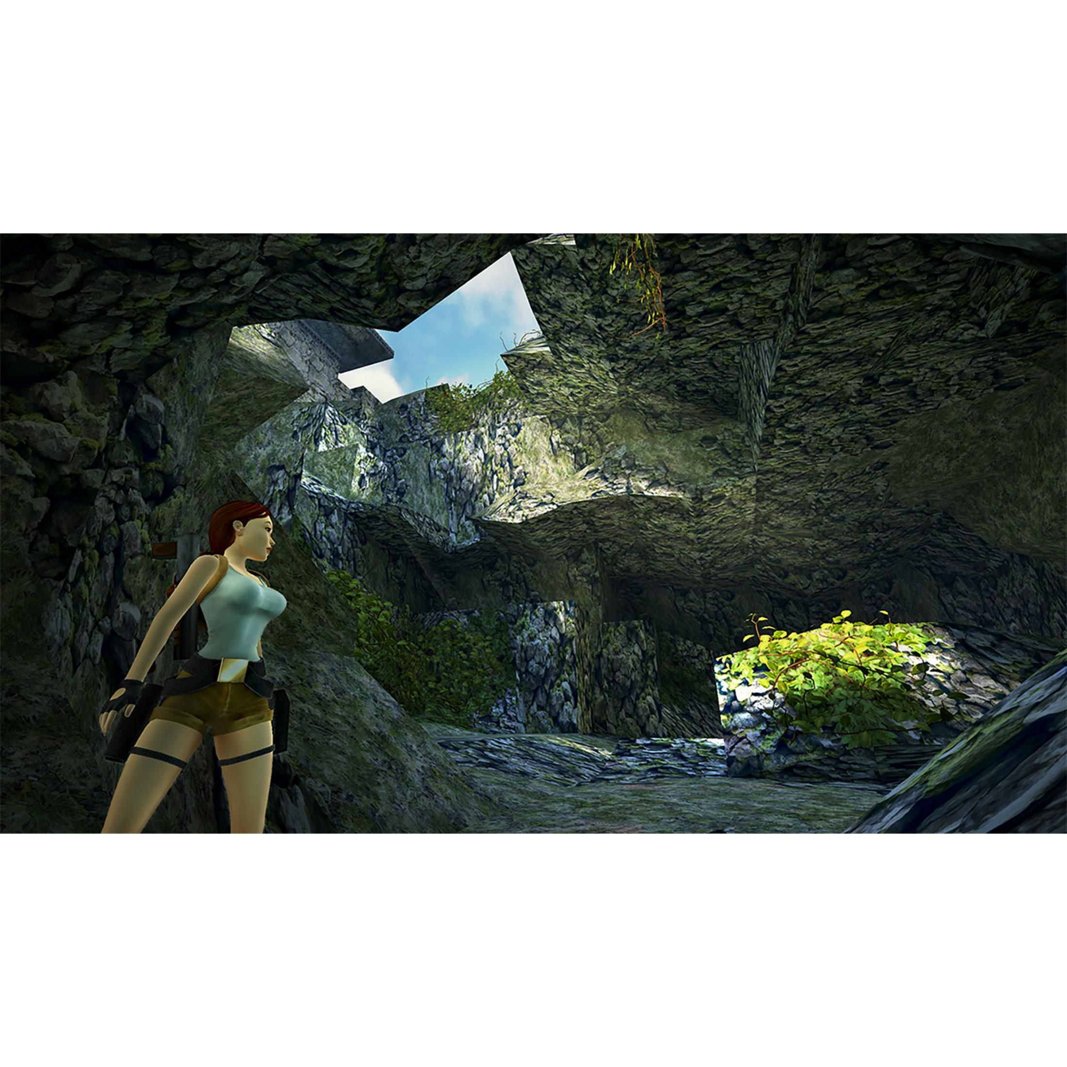 Una donna in top blu e pantaloncini si trova nell'apertura di una grotta muschiosa, guardando fuori.