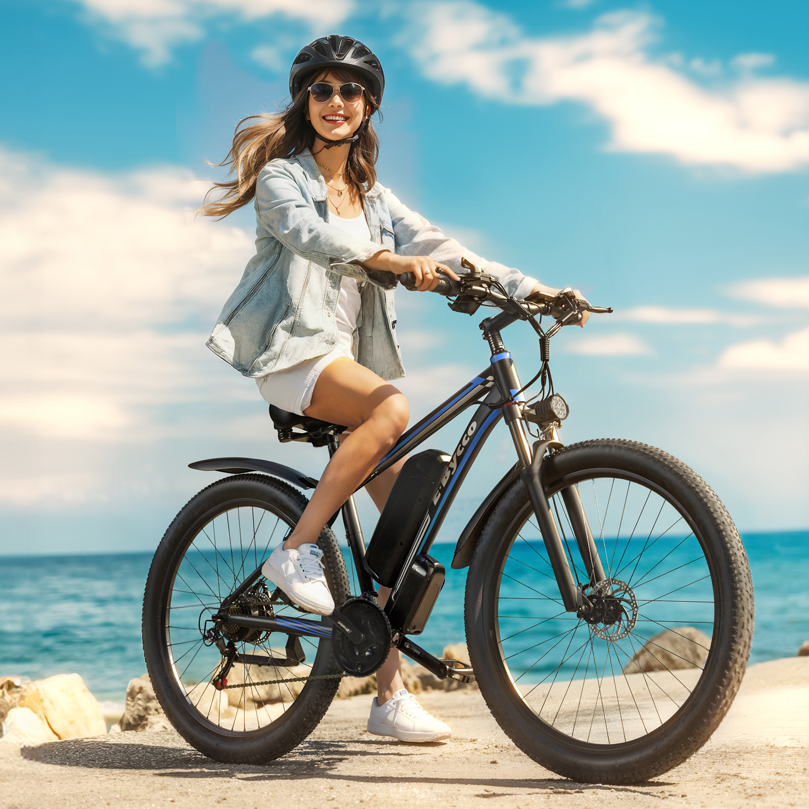 Una mujer con casco monta una e-bike junto al mar.