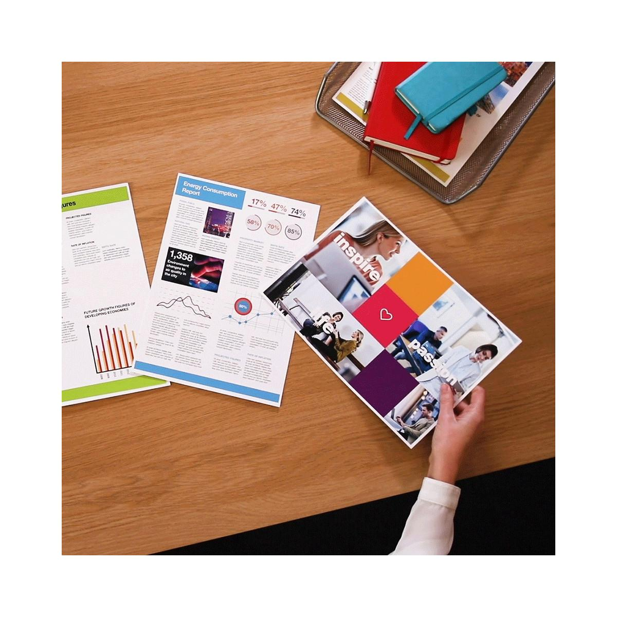A desk with reports, notebooks, and a brochure held by a hand.