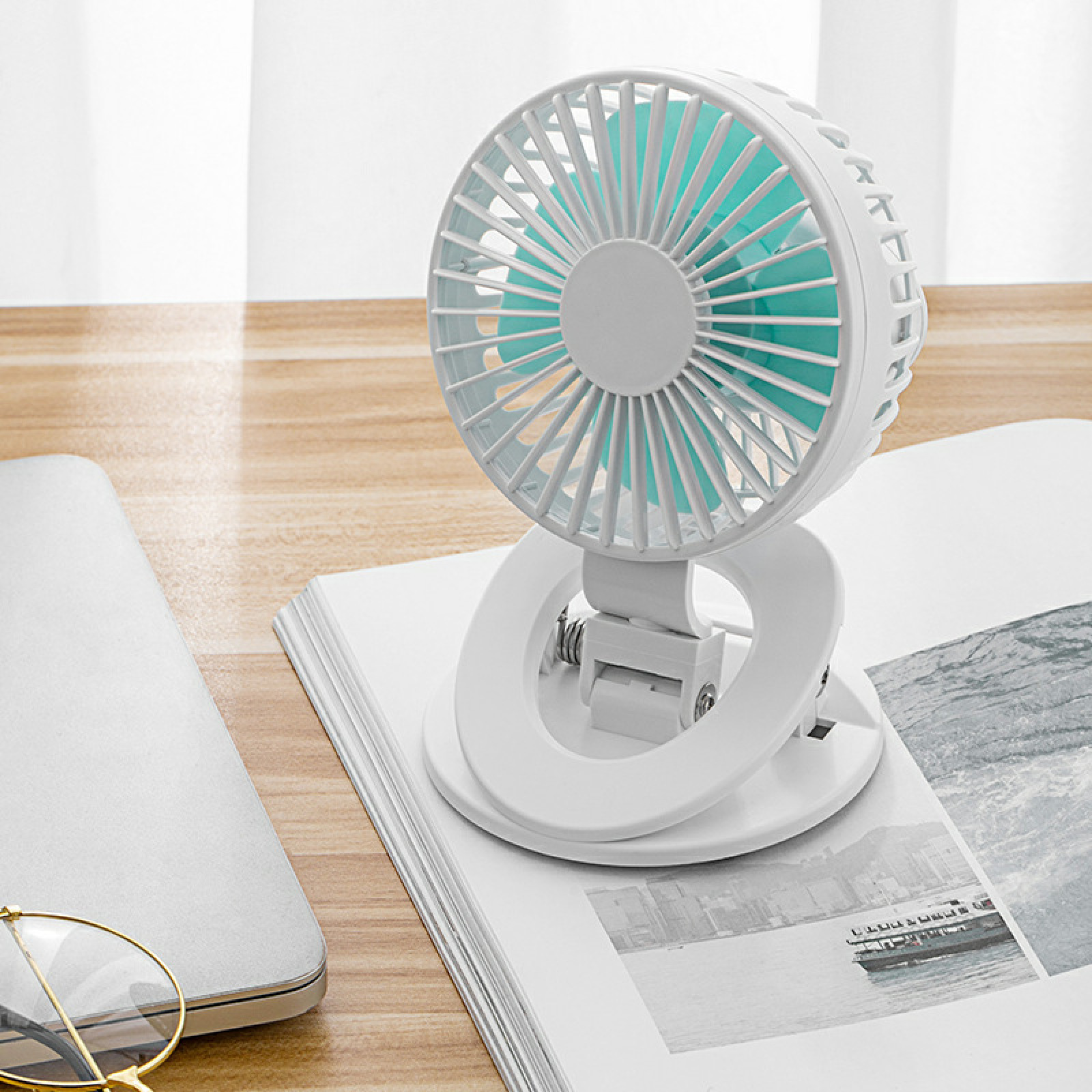 Ein kleiner weißer Ventilator mit türkisen Flügeln steht auf einem Buch.