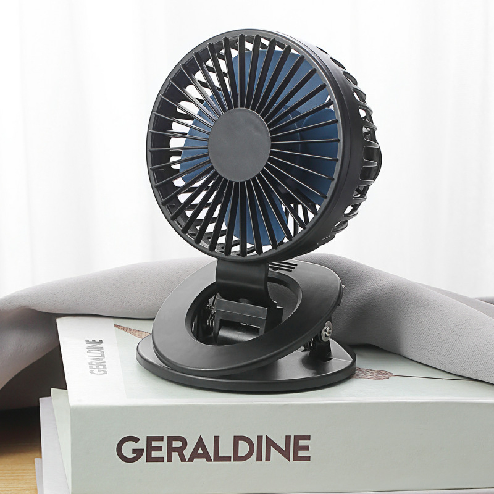 Ein schwarzer Clip-Ventilator mit blauen Rotorblättern steht auf Büchern.