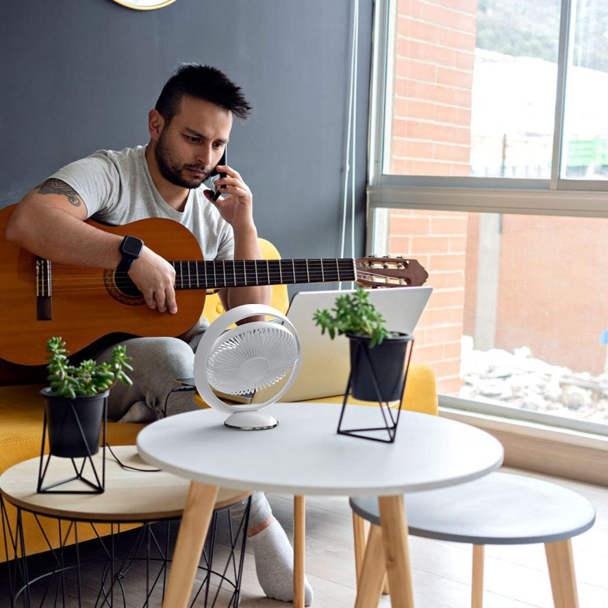 Ein Mann sitzt auf einem gelben Sofa und spielt Gitarre, während er telefoniert.