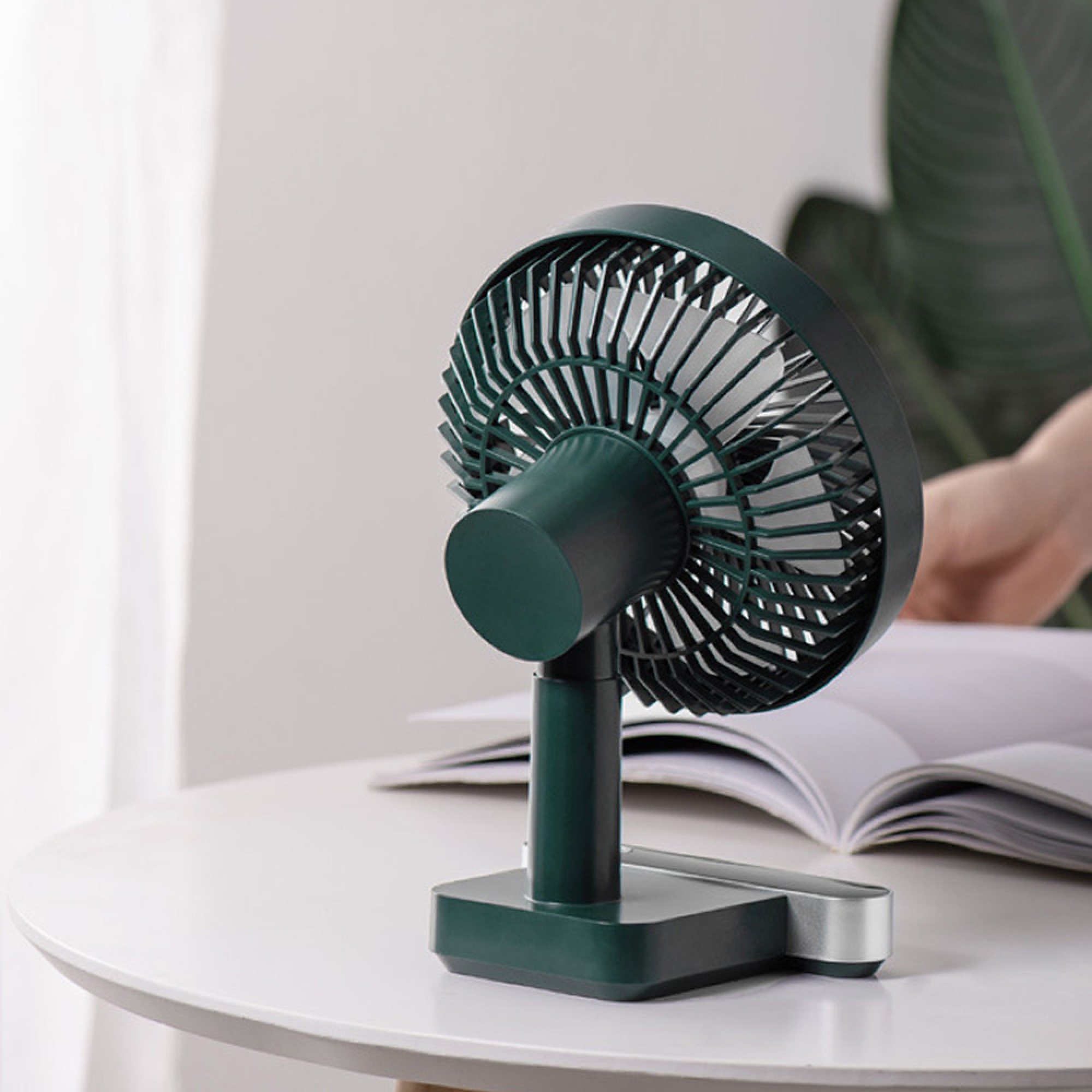 Ein dunkler grüner kleiner Ventilator steht auf einem Tisch neben einem offenen Buch.