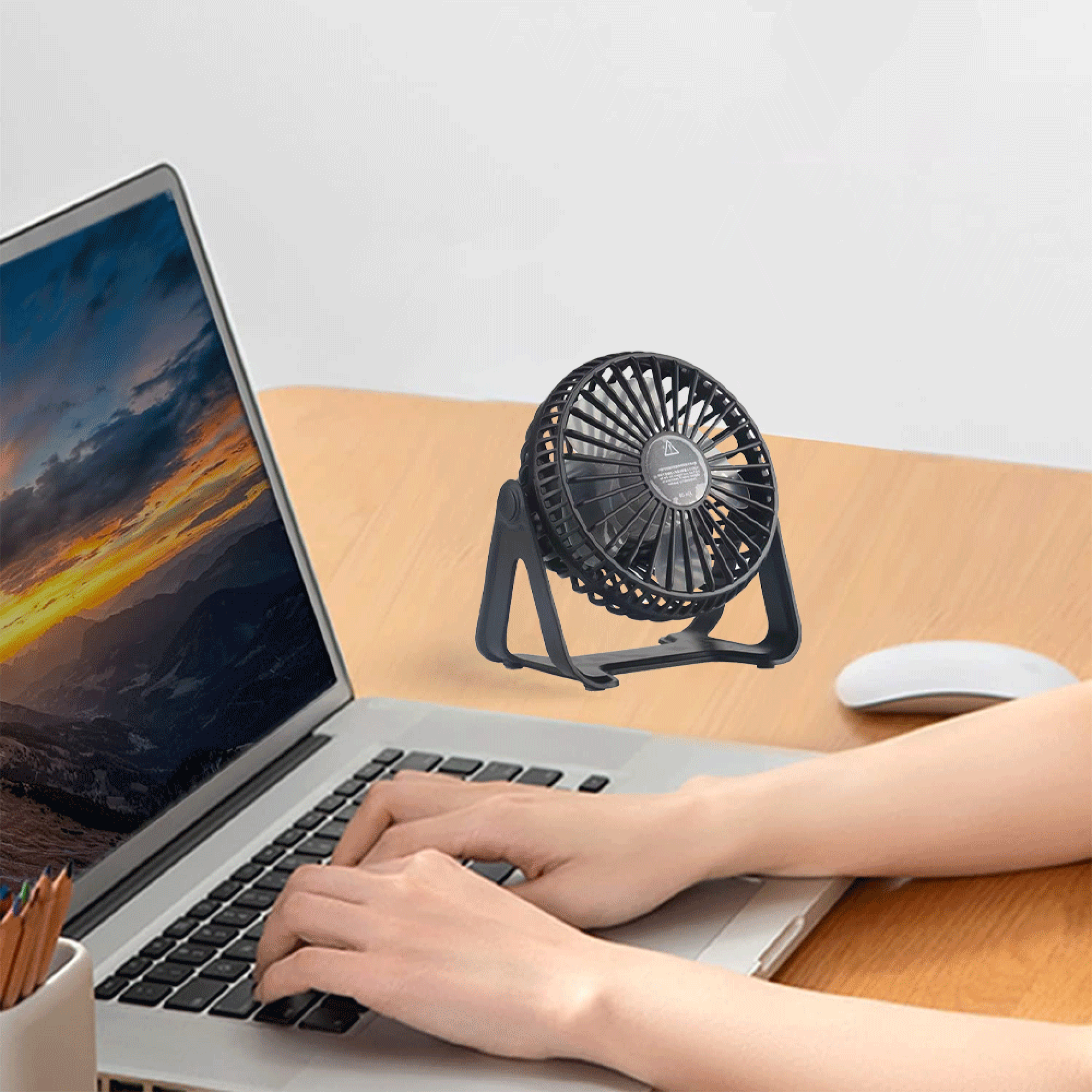Ein schwarzer Mini-Ventilator steht neben einem Laptop auf einem Holzschreibtisch.