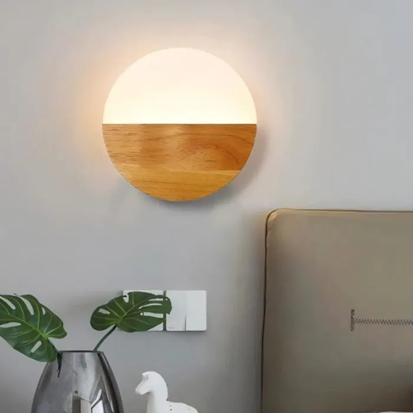 Runder Wandleuchter aus Holz und Weiß, neben einem Bett und Pflanzen.