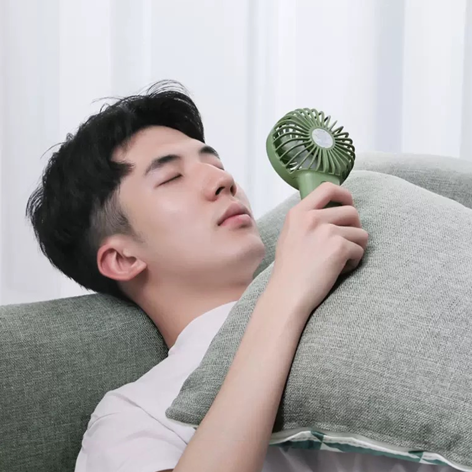 Ein Mann liegt auf einem Sofa und hält einen kleinen grünen Ventilator.