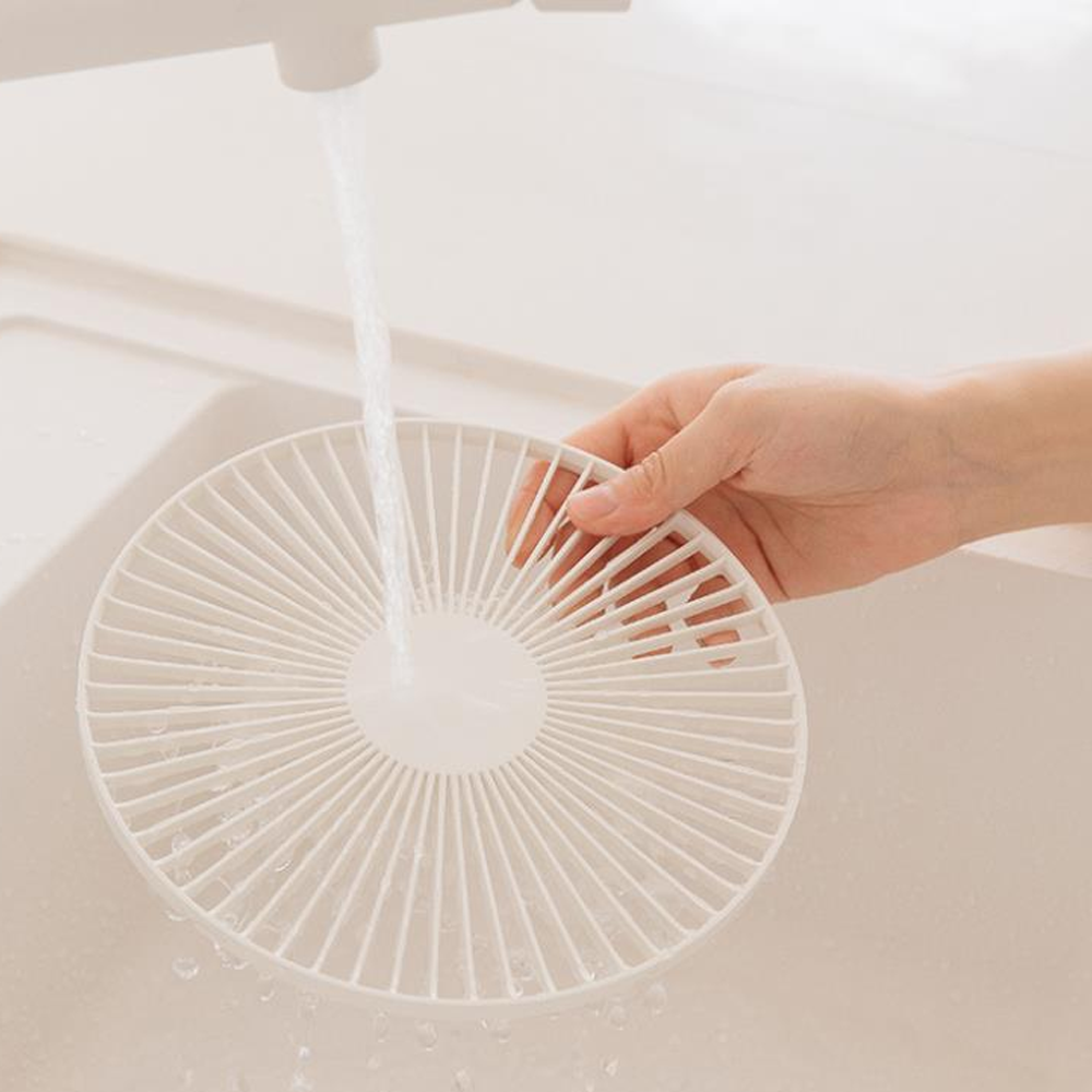 Eine Hand hält einen weißen runden Filter unter fließendem Wasser in einer Spüle.