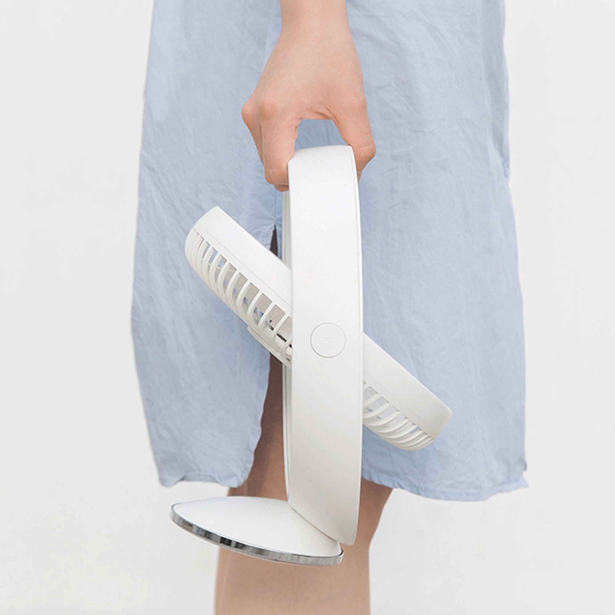 Eine Hand hält einen weißen Ventilator mit silbernem Sockel vor einem blauen Kleid.