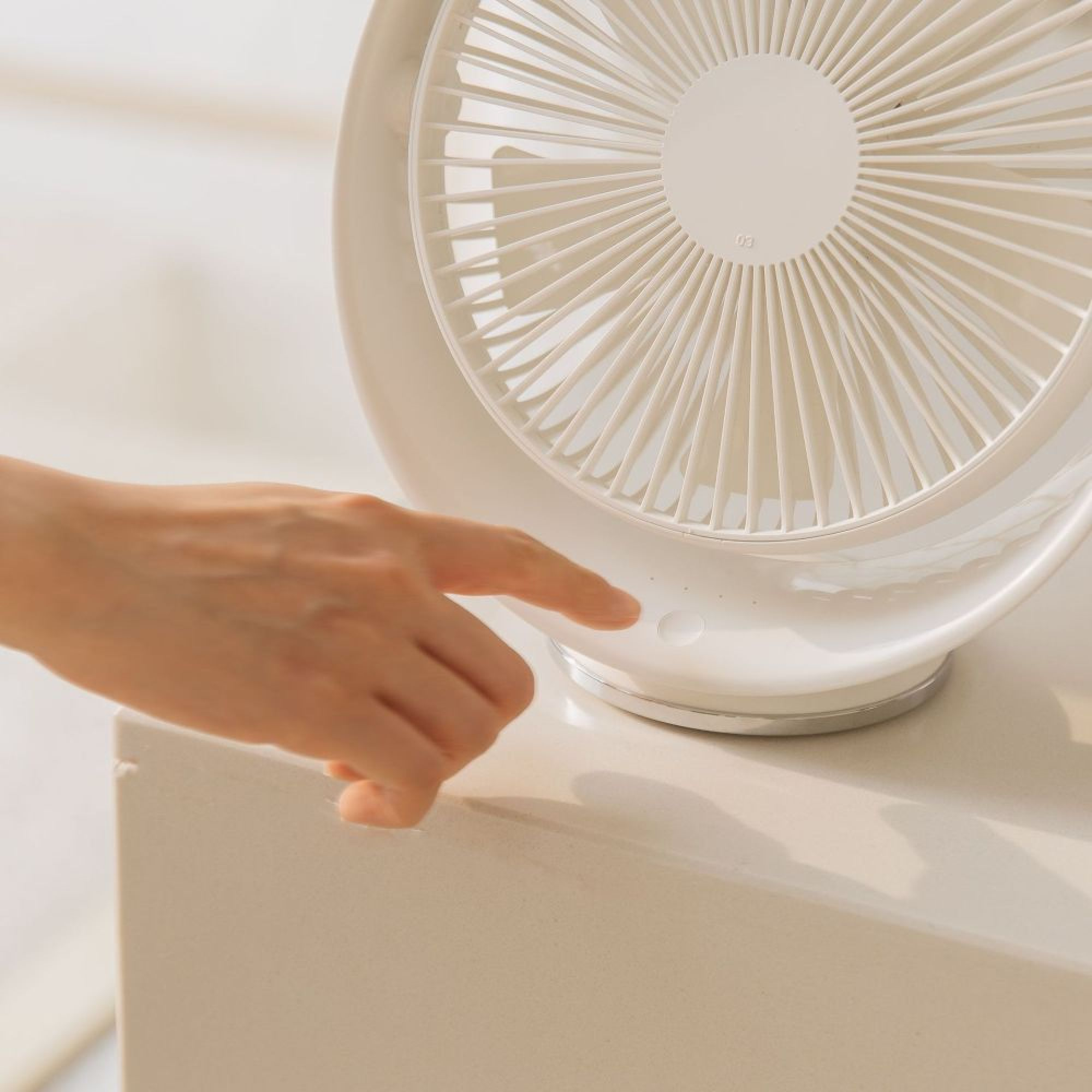Eine Hand drückt einen Knopf auf einem weißen Ventilator.