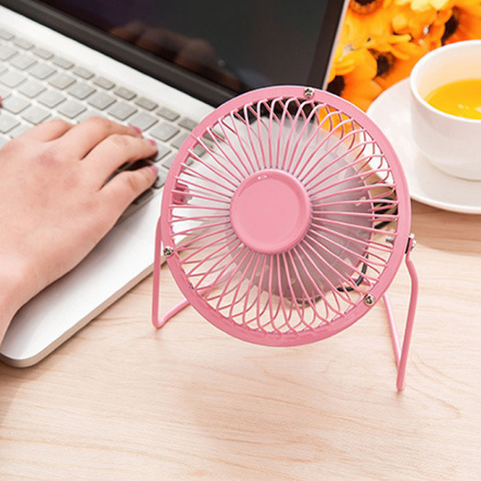 Rosa Schreibtischventilator auf Holzoberfläche neben Laptop und Orangensaft.