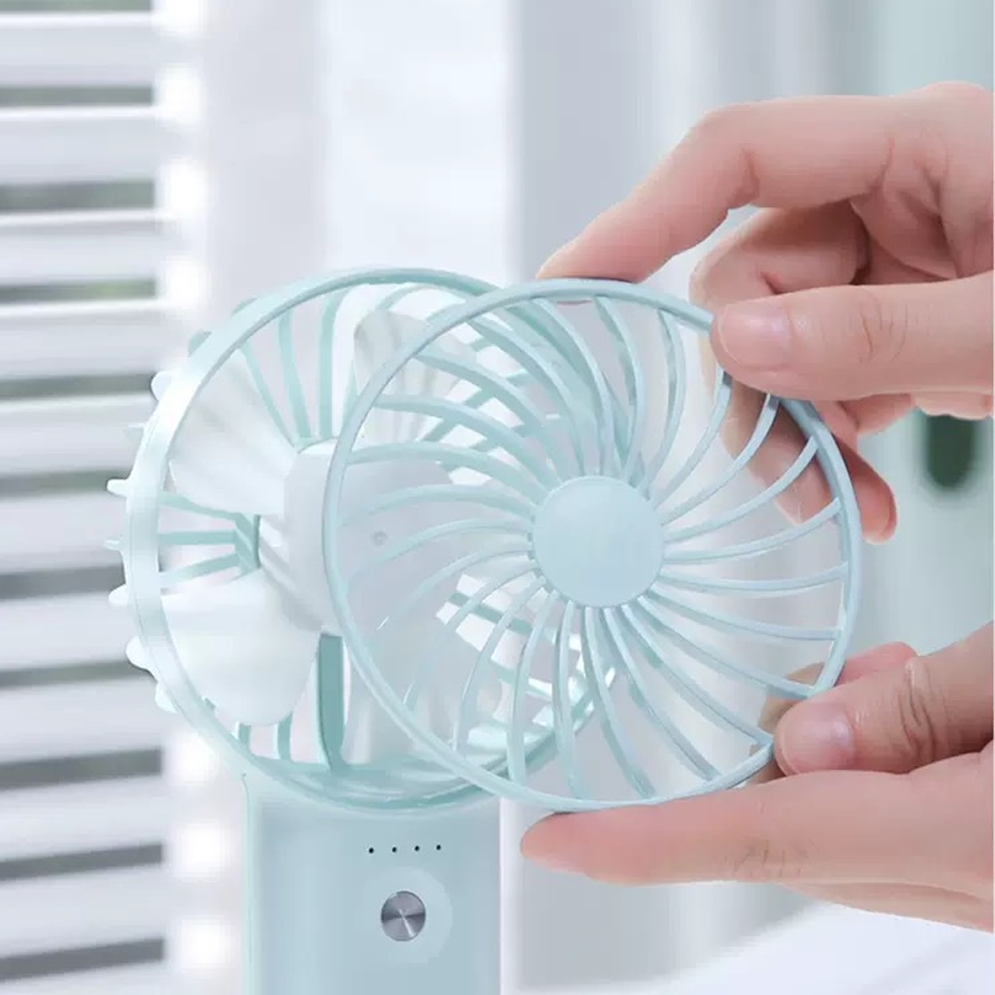 Hände halten einen blauen Ventilator mit weißen Flügeln. Ein Schutzgitter wird abgenommen.