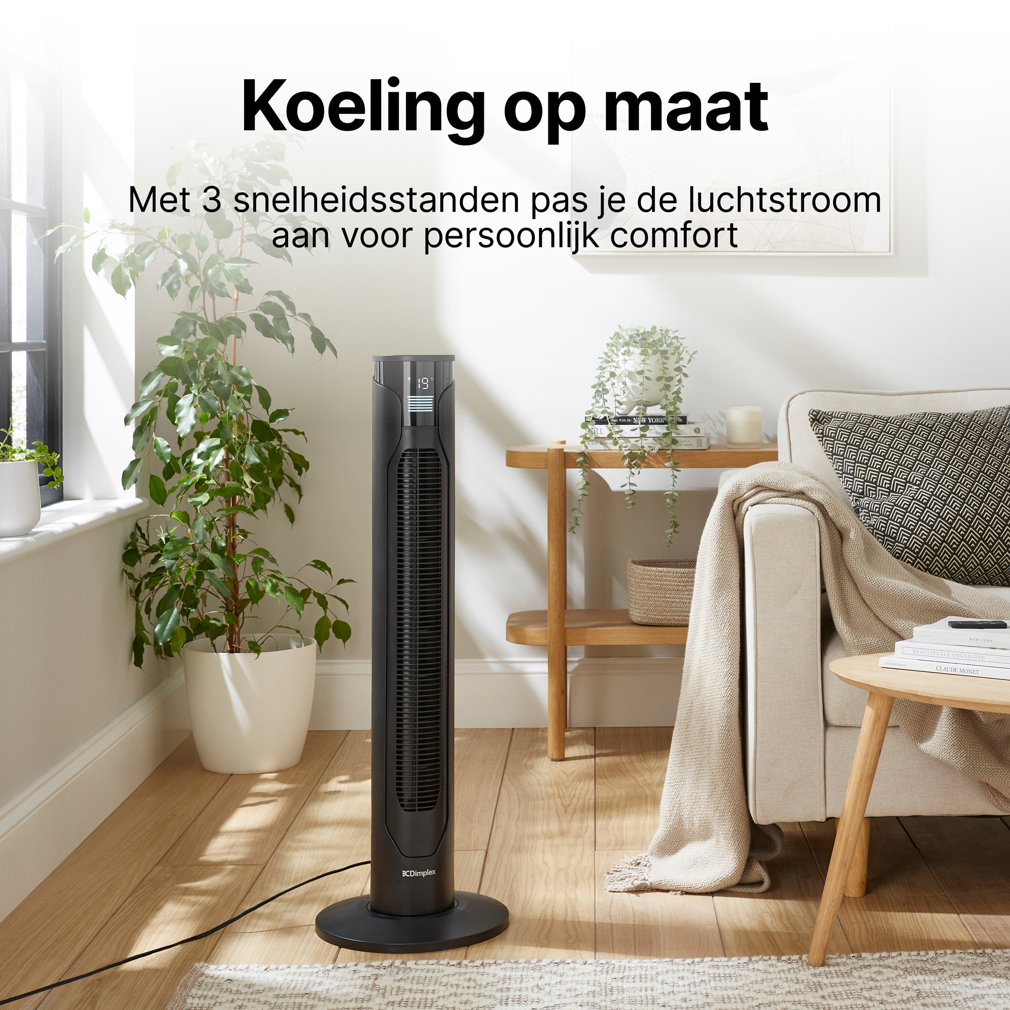 Een zwarte torenventilator staat naast een plant in een woonkamer.